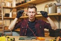 Handsome smiling young man working in carpentry workshop at wooden table place with piece of wood Royalty Free Stock Photo