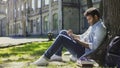 Multinational male sitting under tree using phone, reading newsfeed on gadget