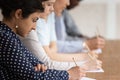 Multinational students seated at desk in row holding pencils writing on papers