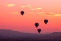 multiple balloons taking flight, pinkorange dawn sky