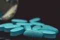 Multiple blue pills spilled from bottle on black background