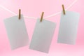 Multiple empty paper sheet for notes that hang on a rope with clothespins and isolated on pink. Blank white photo hanging on rope Royalty Free Stock Photo