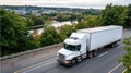 Multiple freight trucks drive on a highway beside a river, with buildings visible in the background under overcast skies Royalty Free Stock Photo