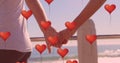 Multiple heart balloons floating against mid section of couple holding hands at beach