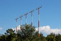 Multiple high metal red and white poles with airport runway guiding lights surrounded with dense trees