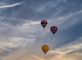 Multiple multi-colored hot air balloons floating in a blue sky with thin clouds.