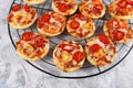 Small mini pizzas topped with cheese, tomato, yellow and red bell peppers and salami sausage on round black grid Royalty Free Stock Photo