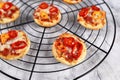 Small mini pizzas topped with cheese, tomato, yellow and red bell peppers and salami sausage on round black grid Royalty Free Stock Photo