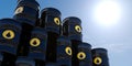 Multiple stacked black metal oil barrels with drop symbols backlit by sun with sky background