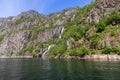 Mossy cliffs of Trollfjorden release waterfalls into the fjord under a sunny sky Royalty Free Stock Photo