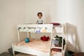 Multiracial boy looking at the camera with happy smile while standing at the second tier of his bed