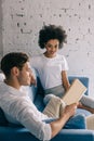 Multiracial boyfriend and girlfriend reading book on sofa