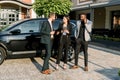 Multiracial business people, two men and one woman have a work meeting outdoors, standing on the background of black car Royalty Free Stock Photo