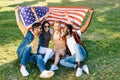multiracial cheerful friends with american flag sitting on green grass