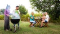 Multiracial couple cooking food on grill for friends. Outdoor garden barbecue party. Friends laughing and having fun. Royalty Free Stock Photo