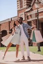 Multiracial couple with shopping bags and taking selfie with smartphone using selfiestick on the street