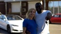 Multiracial couple showing keys against new white luxury car, auto purchase