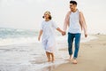 Multiracial couple smiling and holding hands while walking on beach Royalty Free Stock Photo
