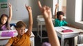 Multiracial elementary school students raising hands during class in classroom Royalty Free Stock Photo