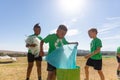 Multiracial elementary schoolboys cleaning plastic in school ground during sunny day
