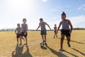 Multiracial elementary schoolboys playing soccer on school soccer field against sky during sunny day