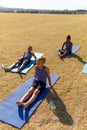 Multiracial elementary schoolboys sitting on exercise mat in school ground during sunny day