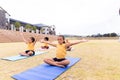 Multiracial elementary schoolgirls with arms outstretched exercising on yoga mat against sky