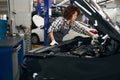 Multiracial female auto repairman looks under hood glass washer reservoir