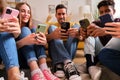 Multiracial friends looking at their mobile phones sitting on a semicircle. Royalty Free Stock Photo