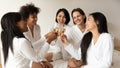 Multiracial girls holding champagne glasses hanging out in hotel bedroom Royalty Free Stock Photo