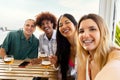 Multiracial group of friends taking selfie looking at camera while having drinks together at beach bar. Royalty Free Stock Photo