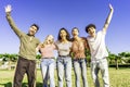 Multiracial group of young friends posing with raised open arms looking at camera embracing to each other in nature of city park. Royalty Free Stock Photo