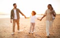 Multiracial parents walking on beach with two sons, holding hands and smiling, enjoying evening by seaside, full length Royalty Free Stock Photo