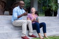 Multiracial senior couple having coffee while sitting on steps outside house Royalty Free Stock Photo