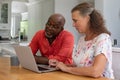 Multiracial senior couple using laptop while sitting at table in living room Royalty Free Stock Photo