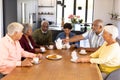 Multiracial senior friends having coffee and cookies while sitting at dining table in nursing home Royalty Free Stock Photo