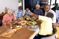 Multiracial senior woman showing smart phone to friends while having lunch at dining table Royalty Free Stock Photo