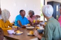 Multiracial seniors looking at happy woman serving juice to man at dining table in retirement home Royalty Free Stock Photo