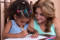 Multiracial small girl and her mother drawing with color pencils