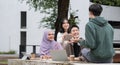 Multiracial smiling group of teenage student using laptop doing homework and enjoying a relaxed atmosphere outdoors at