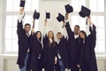 Multiracial students stand in a classroom and look up at their raised hands with mortar boards. Royalty Free Stock Photo