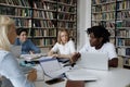 Multiracial students studying together sit at table in university library