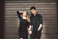 Multiracial stylish couple in black clothes posing on a background of a wooden wall. Turkish guy and caucasian girl date and love