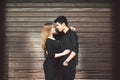 Multiracial stylish couple in black clothes posing on a background of a wooden wall. Turkish guy and caucasian girl date and love