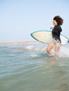Multiracial surfer girl running to the waves on the beach shore Royalty Free Stock Photo