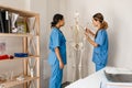 Multiracial women doctors talking while examining skeleton in office