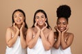 Multiracial women in towels touch cheeks, beige studio background Royalty Free Stock Photo