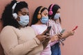 Multiracial women using mobile smartphone and listening music with wireless headphones while wearing face mask during coronavirus Royalty Free Stock Photo