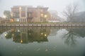 Multistory modern house apartment building reflection, fall leaves in foggy morning mist along Erie Canal riverside walk in Royalty Free Stock Photo