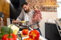 Multitasking father babysitting, cooking breakfast and talking on smart phone at home. Royalty Free Stock Photo